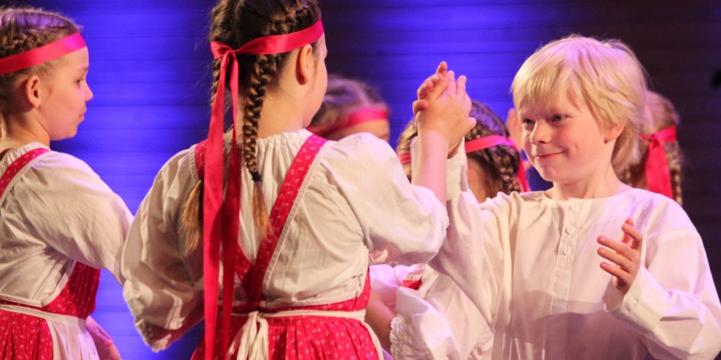Lapset tanssivat kansantanssia puna-valkoisissa asuissa.